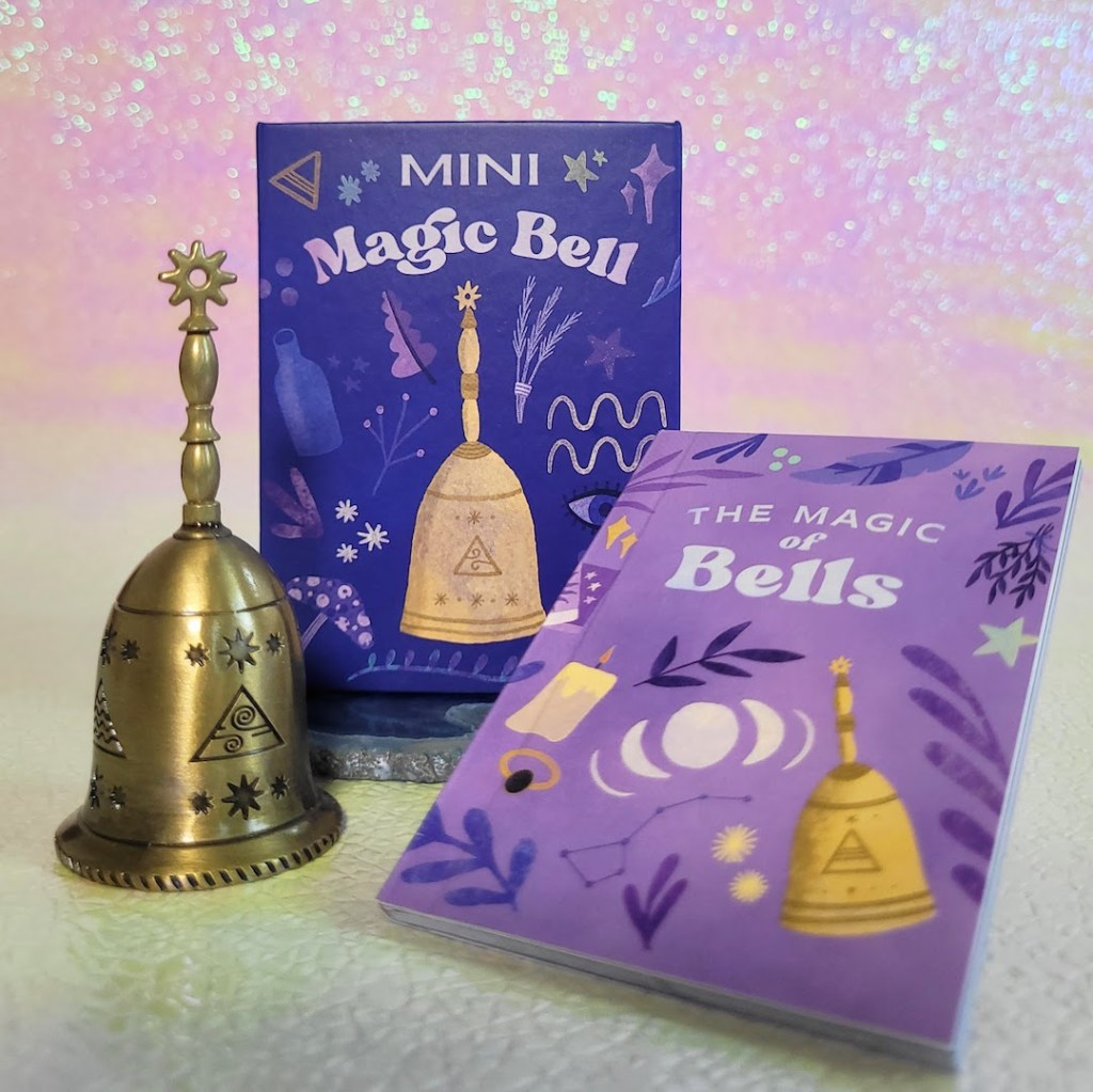 Photo of the "Mini Magic Bell" box, bell, and included guidebook against a pink and yellow iridescent background