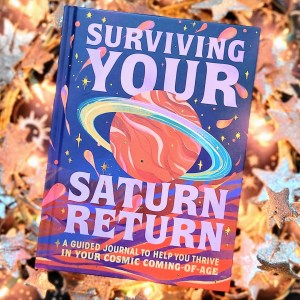 Photo of "Surviving Your Saturn Return" laid above softly lit holiday and starry decor