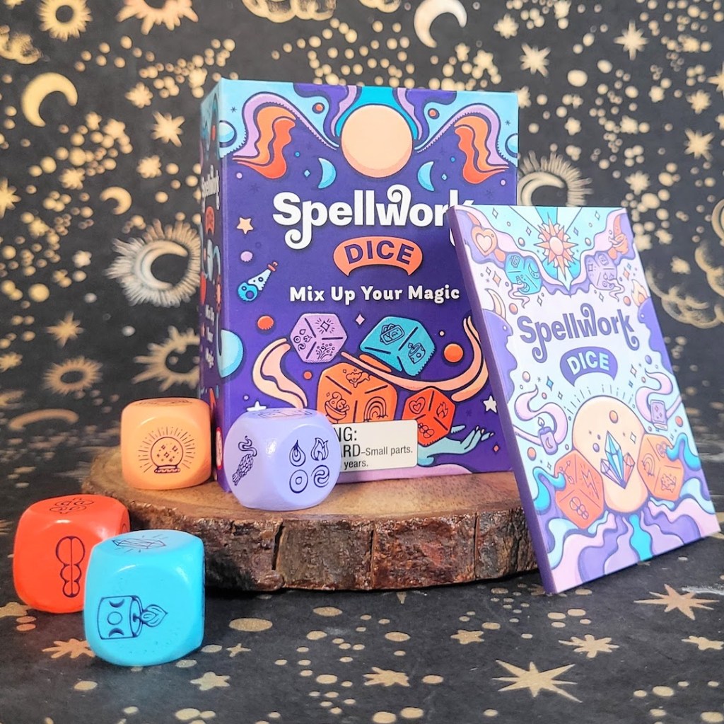 Photo of the "Spellwork Dice" box, dice, and included guidebook standing against a dark starry backdrop