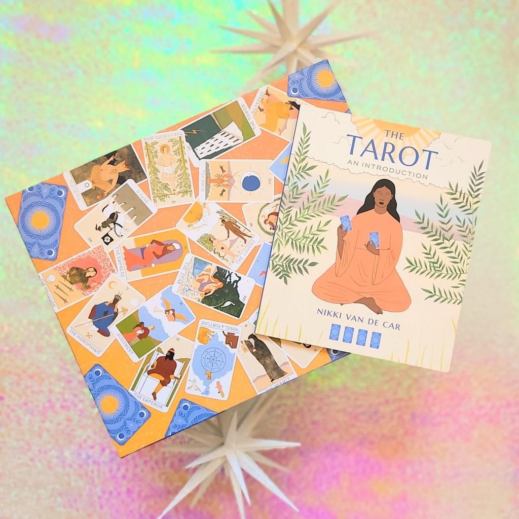Photo of "Tarot 500-Piece Puzzle" box and included mini book laid above a pink and green iridescent background, surrounded by decorative starbursts.
