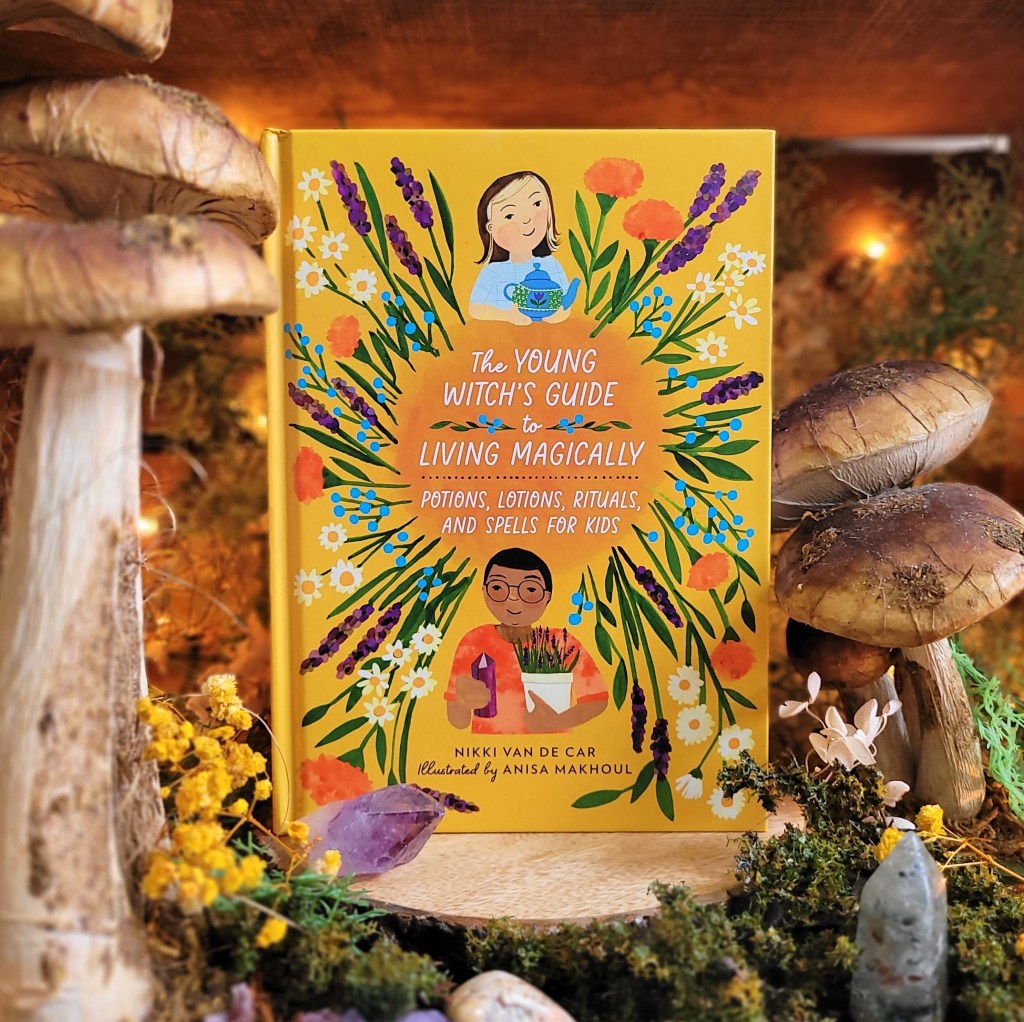 Photo of "The Young Witch's Guide to Living Magically" standing among decorative mushrooms and floral decor with soft amber lighting