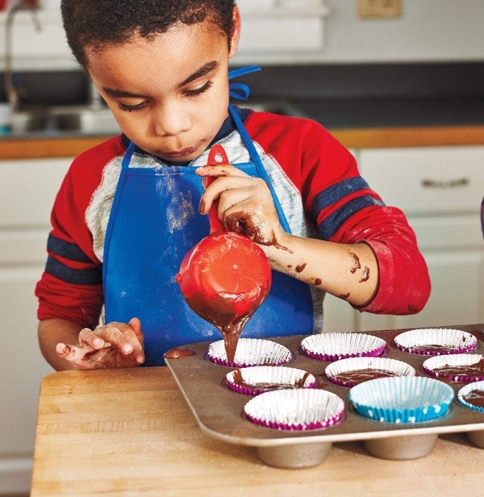 Child pouring cupcake batter into a muffin pan.