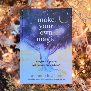 Photo of “make your own magic: a beginner’s guide to self-empowering witchcraft” laid above softly lit starry decor against a dark background