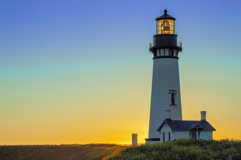 Image of lighthouse with striated blue, turquoise, and yellow sunset behind it.