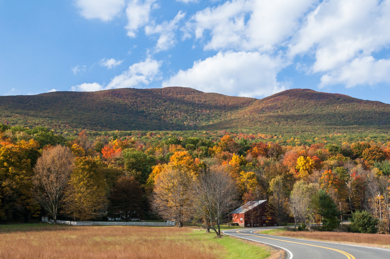 A winding country road through low mountains with fall trees and a barn.