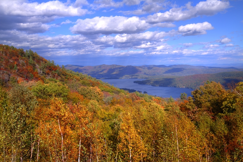 Image from mountain overlook of colorful fall valley with big blue lake under white puffy clouds.