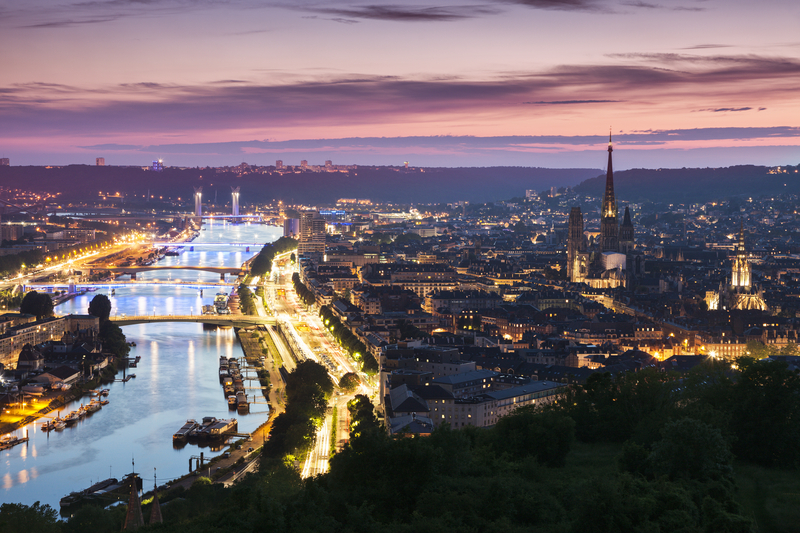 Illuminated city skyline and the banks of a river glowing under pink and purple sky