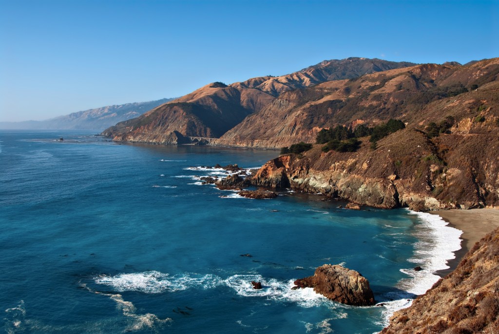 Rolling brown coastal hills along blue ocean under blue sky