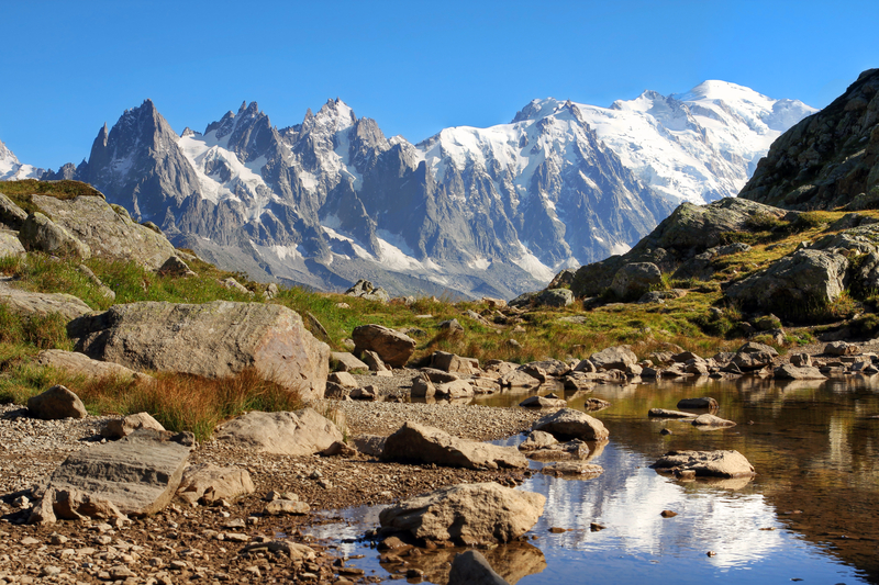 Snowcapped mountains above a rocky green tundra and reflected in pool of water