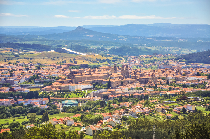 Landscape photo of a town with red roofed buildings amid rolling green hills and mountains