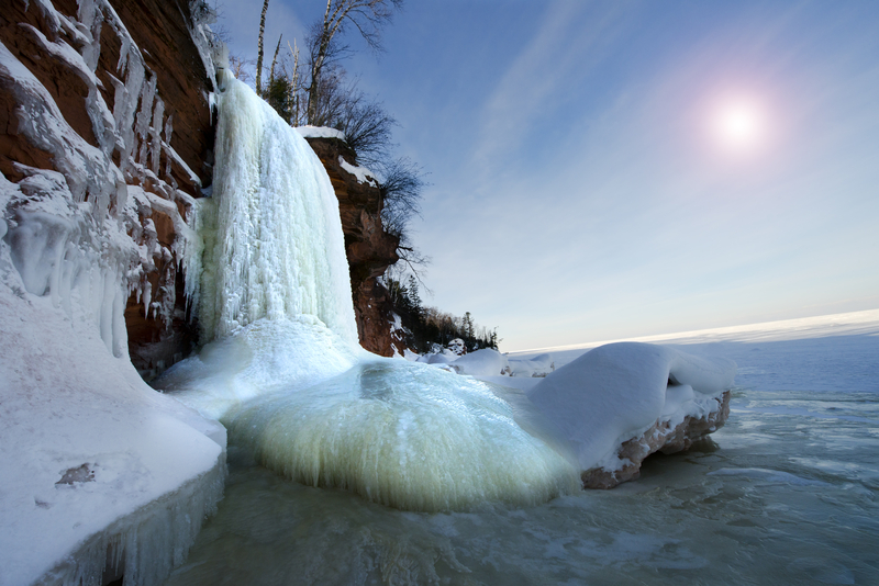 a frozen waterfall pouring off a rocky bluff onto a frozen lake surface