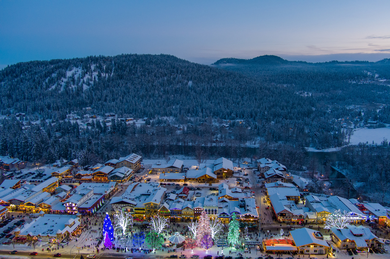 Aerial view of town lit up by Christmas lights and surrounded by mountains stretching into the distance at dusk