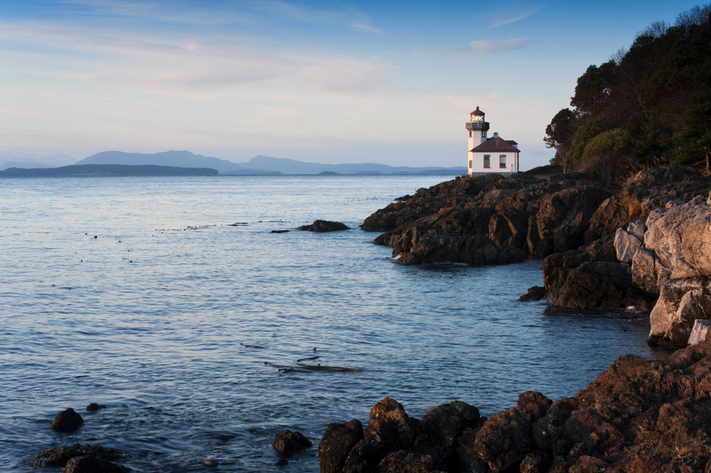 A white lighthouse on a rocky promontory with trees next to ocean cove