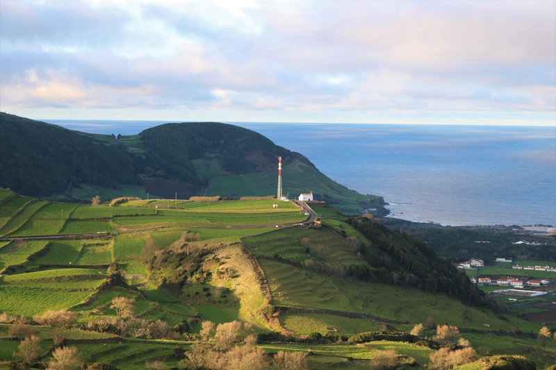 Landscape of lush green fields on a plateau looking out over a coastal village next to the sea