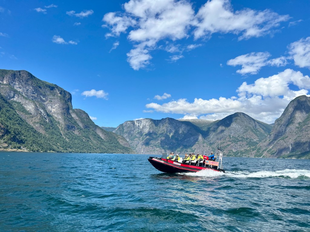 A red boat travels through a fjord on a sunny day
