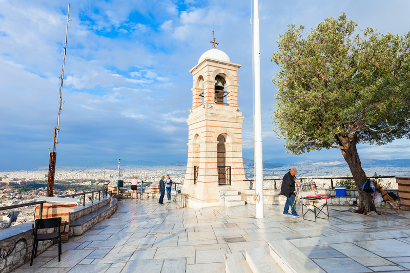 A stone courtyard and tower at the top of a mountain with city view in the distance