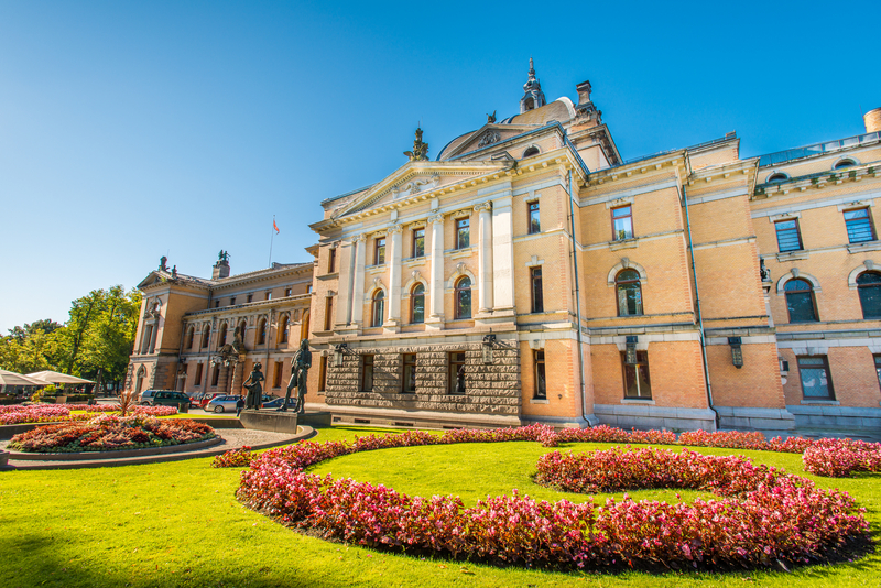 A large, stately stone building with landscaped, swirling garden of red flowers in front of it