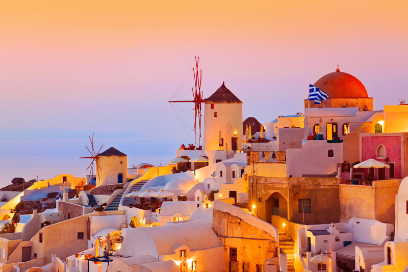 A whitewashed village and windmills on a hill under pink and orange sunset