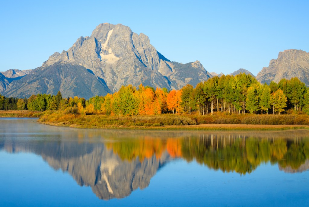 a mountain surrounded by fall foliage trees, next to a lake