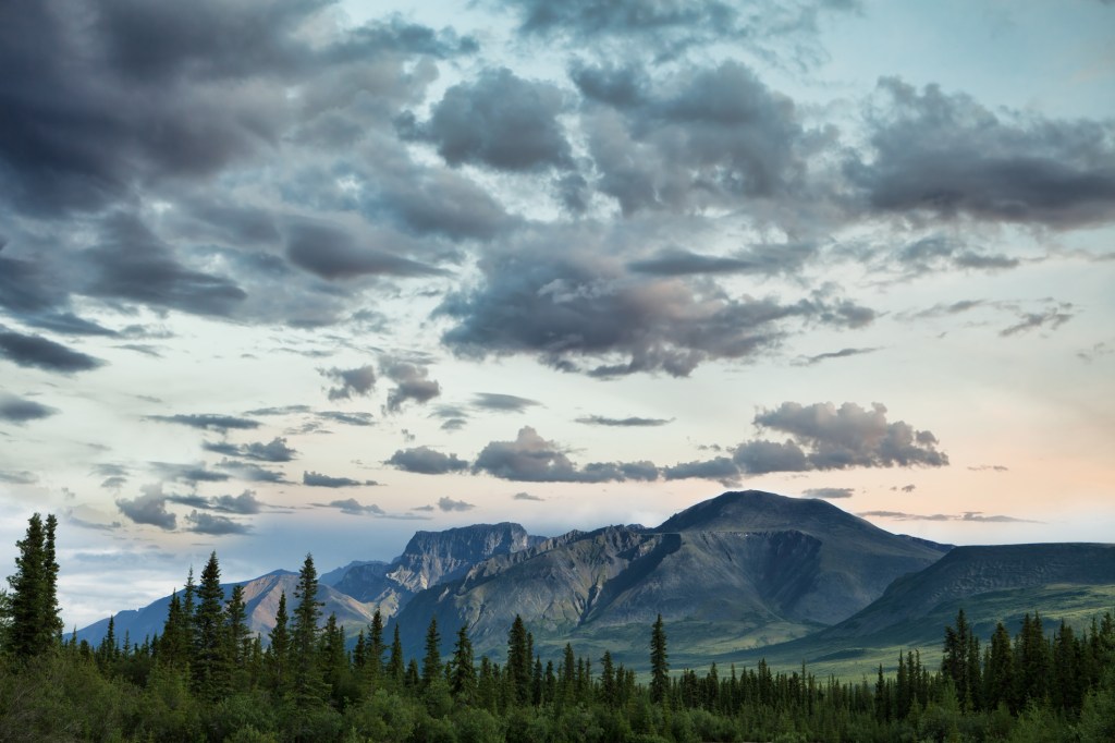 Sunset sky with clouds over mountains with trees in the foreground