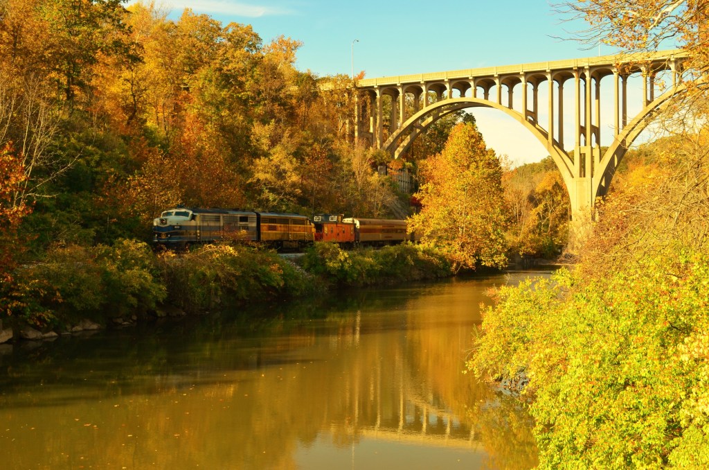 a railroad runs under an arch bridge, next to a river