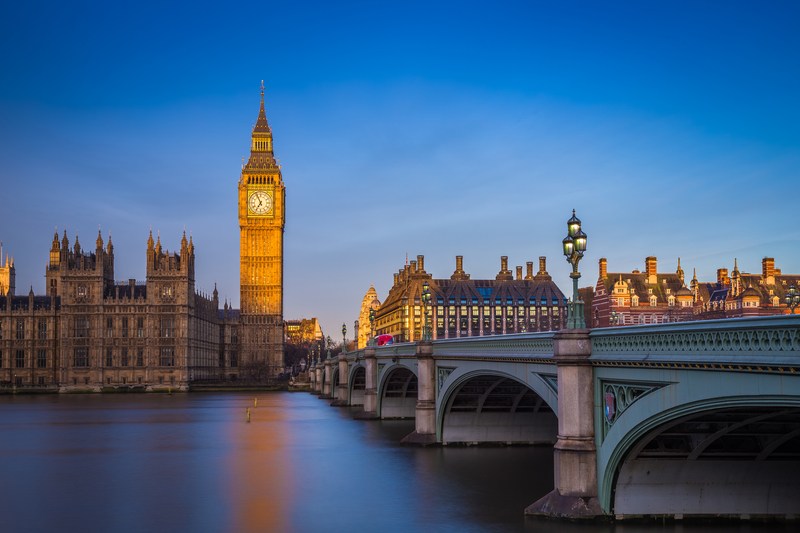Image of bridge and clock tower at sunrise under clear dark blue sky