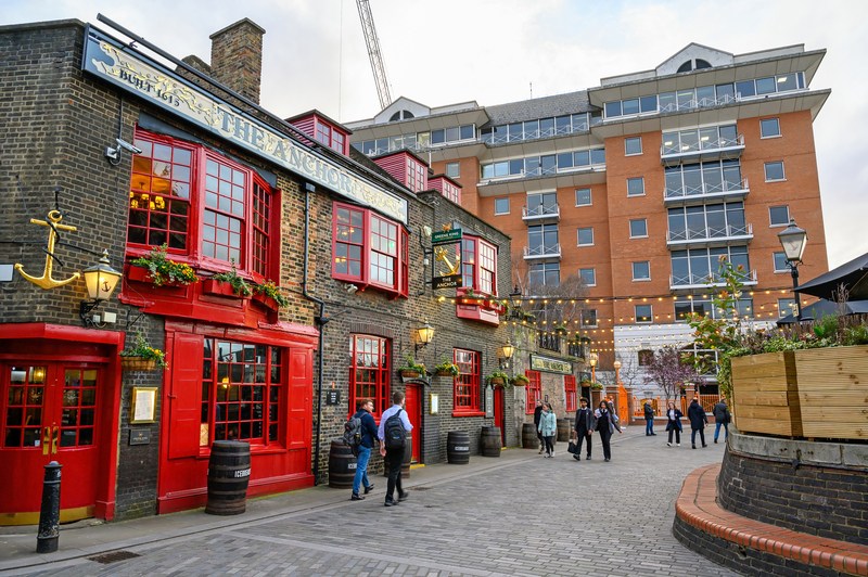A brick pub with red windows and doors on a cobblestone street with people walking by